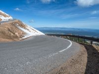 a man is riding his bike down a mountain road with snow and rocks in the background