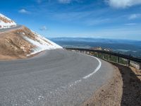 a man is riding his bike down a mountain road with snow and rocks in the background