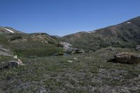 a view of a grassy mountain valley with two little lakes in the foreground and large snow mountains in the back