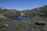 a view of a grassy mountain valley with two little lakes in the foreground and large snow mountains in the back