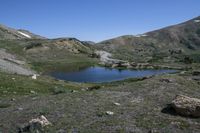 a view of a grassy mountain valley with two little lakes in the foreground and large snow mountains in the back