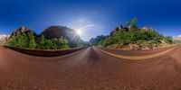 a 360 - view photo of the road through a mountain valley and the sun shining down