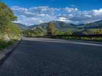 the road winds up on the mountainside on a sunny day with beautiful clouds and trees