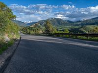 the road winds up on the mountainside on a sunny day with beautiful clouds and trees