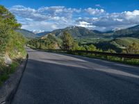 the road winds up on the mountainside on a sunny day with beautiful clouds and trees