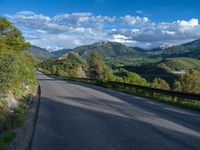 the road winds up on the mountainside on a sunny day with beautiful clouds and trees