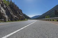 an asphalt road going to the mountains with rocks in the distance and a highway sign above it