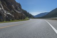 an asphalt road going to the mountains with rocks in the distance and a highway sign above it