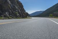 an asphalt road going to the mountains with rocks in the distance and a highway sign above it