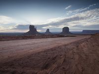 a wide view of a desert with rocks and sand at sunset with the setting sun in the middle of it