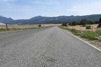 a man walks along a paved road towards the mountains in the distance, with no cars on the roadway