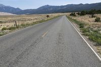 a man walks along a paved road towards the mountains in the distance, with no cars on the roadway