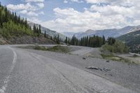 a motorcycle is riding on the road down to the mountain side by itself with trees on both sides, on a road, in the mountains and the distance are other mountains