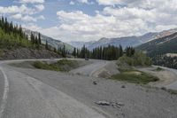 a motorcycle is riding on the road down to the mountain side by itself with trees on both sides, on a road, in the mountains and the distance are other mountains