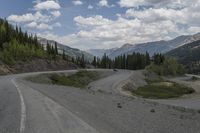 a motorcycle is riding on the road down to the mountain side by itself with trees on both sides, on a road, in the mountains and the distance are other mountains