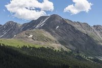 the view of a valley from near mountains under blue skies with clouds and trees on a sunny day