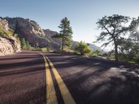 there is a long stretch of road in the mountains near some rocks and trees and some rocks