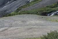 a sheep is walking near the mountainside with a waterfall nearby as the animal wanders