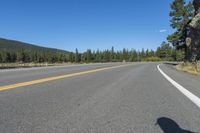 a cyclist taking a photo on a paved highway near trees and mountain with bright blue sky