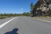 a cyclist taking a photo on a paved highway near trees and mountain with bright blue sky