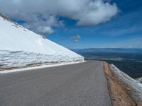 a snow covered road is near a very steep cliff on a clear day the wall is filled with snow and snow