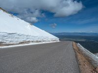 a snow covered road is near a very steep cliff on a clear day the wall is filled with snow and snow