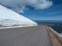 a snow covered road is near a very steep cliff on a clear day the wall is filled with snow and snow