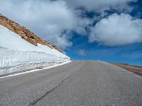 a snow covered road is near a very steep cliff on a clear day the wall is filled with snow and snow