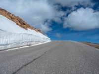 a snow covered road is near a very steep cliff on a clear day the wall is filled with snow and snow