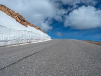 a snow covered road is near a very steep cliff on a clear day the wall is filled with snow and snow