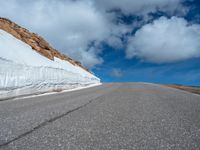 a snow covered road is near a very steep cliff on a clear day the wall is filled with snow and snow