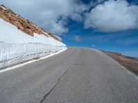 a snow covered road is near a very steep cliff on a clear day the wall is filled with snow and snow