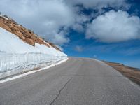 a snow covered road is near a very steep cliff on a clear day the wall is filled with snow and snow