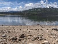 a lake with rocks on the shore and mountains in the background along side it and snow capped hills