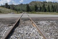 railroad tracks on a gravel road with mountains in the distance in the background and trees,