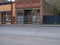 a red fire hydrant sitting in front of an old store window and building next to an open air field