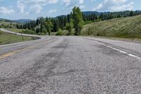 an empty road on a grassy hill surrounded by trees and mountains is seen in this picture