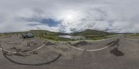 a car driving on the road by a lake on a sunny day and cloudy sky