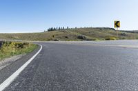 a single lane road with two yellow and black signs beside it and a grassy hill in the background