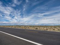 the lone empty asphalted road leads into the vast landscape of a mountainous landscape in southern nevada