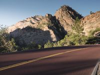 two yellow painted lines on the road that is empty, leading into mountains and greenery