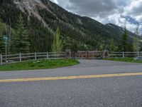 road in the mountains with grass and trees and a fence surrounding it on a bright day