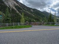 road in the mountains with grass and trees and a fence surrounding it on a bright day