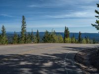 the mountains are visible in the distance from this wide, empty road, overlooking a wide landscape and forest