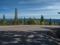 the mountains are visible in the distance from this wide, empty road, overlooking a wide landscape and forest