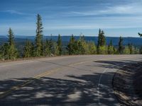 the mountains are visible in the distance from this wide, empty road, overlooking a wide landscape and forest