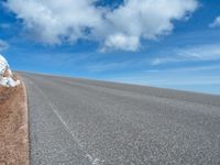 a man is riding his bike down a mountain road with snow and rocks in the background