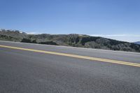 an empty road with pine trees on the side of it and hills in the background