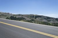 an empty road with pine trees on the side of it and hills in the background