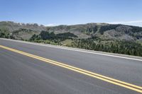 an empty road with pine trees on the side of it and hills in the background